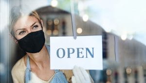 A Shop Assistant Wearing a Mask Holds a Sign Saying Open 